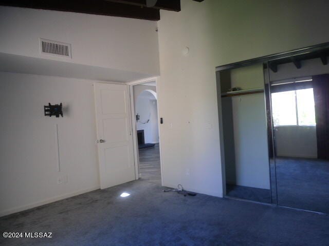 unfurnished bedroom with a high ceiling, a closet, and dark carpet