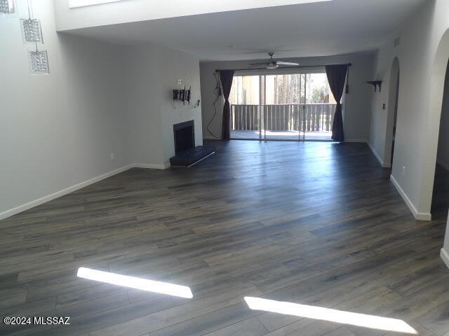 unfurnished living room featuring ceiling fan and dark wood-type flooring