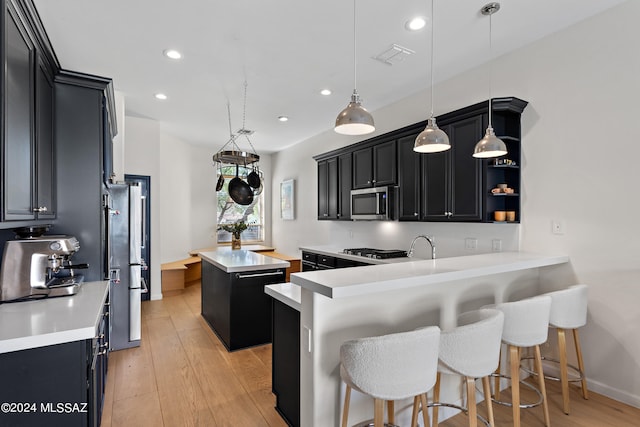 kitchen with pendant lighting, appliances with stainless steel finishes, a center island, a breakfast bar area, and light hardwood / wood-style floors