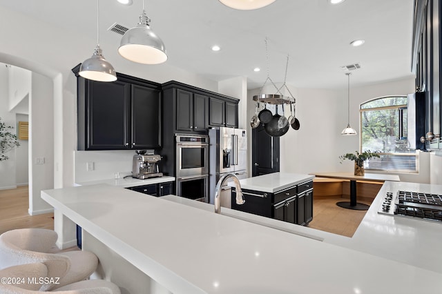 kitchen with light hardwood / wood-style floors, pendant lighting, a breakfast bar area, stainless steel appliances, and kitchen peninsula