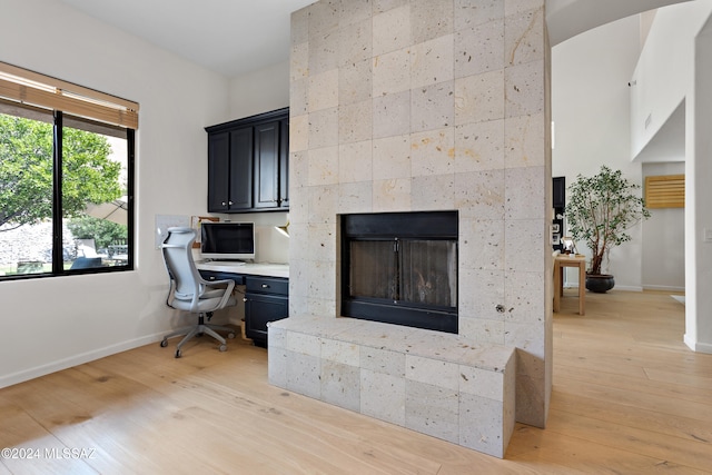 office space featuring light wood-type flooring, built in desk, and a tiled fireplace