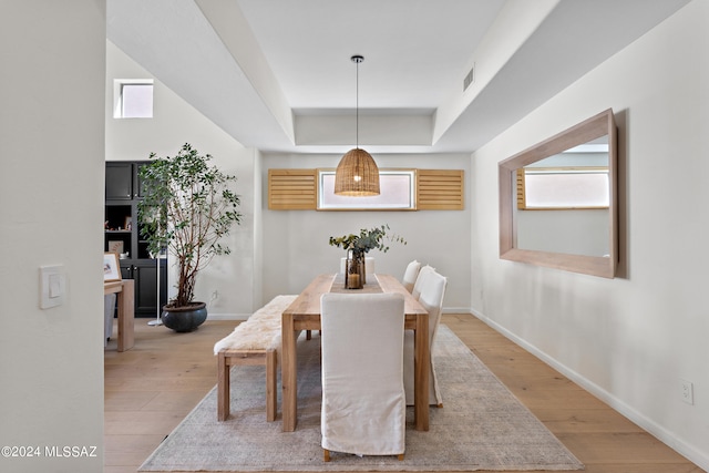 dining space with a raised ceiling, plenty of natural light, and light wood-type flooring