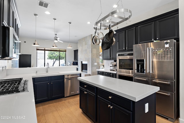 kitchen with a kitchen island, light wood-type flooring, ceiling fan, pendant lighting, and appliances with stainless steel finishes