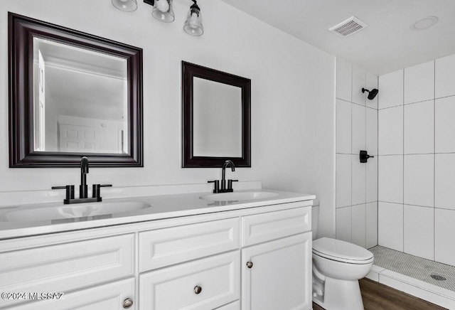 full bathroom with visible vents, a sink, a tile shower, and toilet