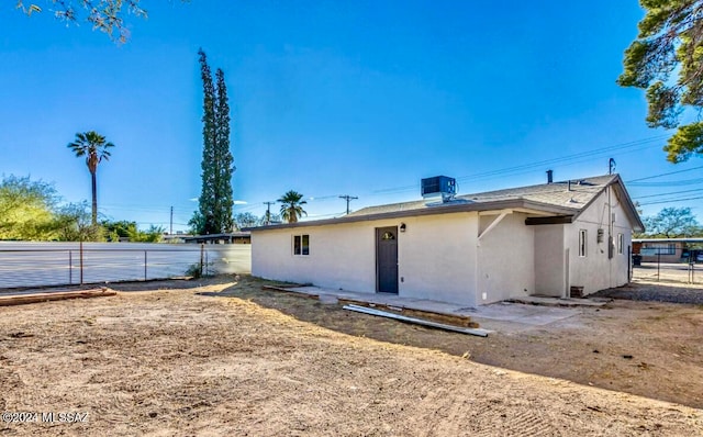 rear view of property with central AC unit, fence, and stucco siding