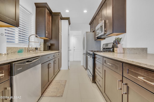 kitchen featuring stainless steel appliances, dark brown cabinetry, light stone counters, and sink