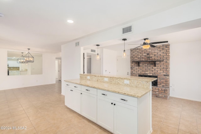 kitchen featuring a brick fireplace, ceiling fan with notable chandelier, light stone countertops, hanging light fixtures, and white cabinets