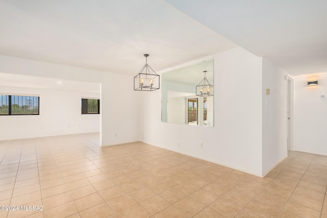 tiled spare room featuring an inviting chandelier