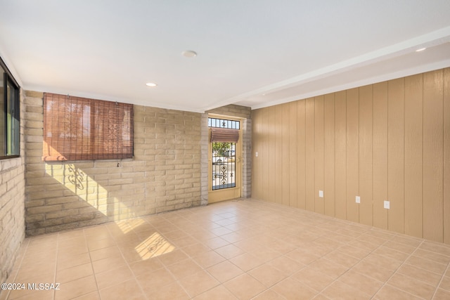 unfurnished room featuring brick wall, light tile patterned flooring, and wood walls