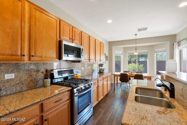 kitchen with sink, light stone countertops, hanging light fixtures, and appliances with stainless steel finishes