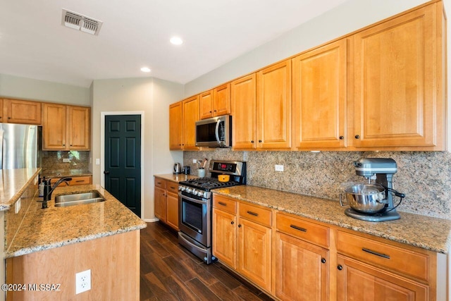 kitchen with appliances with stainless steel finishes, an island with sink, sink, dark hardwood / wood-style flooring, and light stone countertops