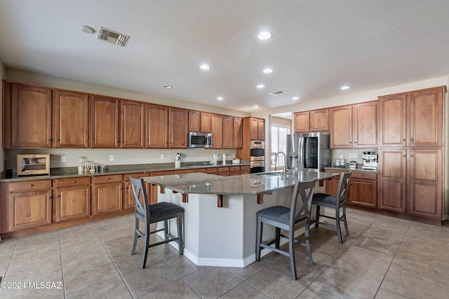 kitchen featuring dark stone counters, a center island with sink, sink, a kitchen bar, and stainless steel appliances