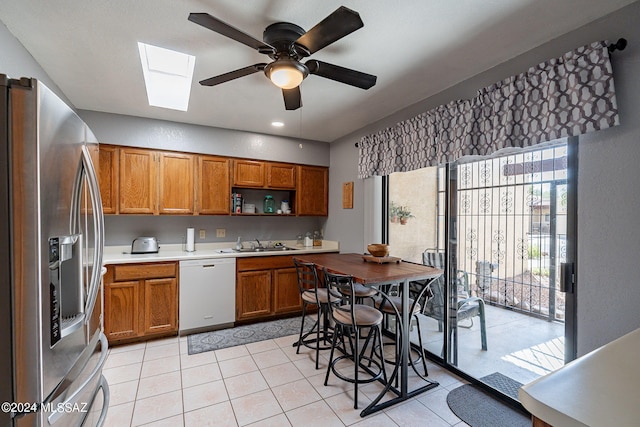 kitchen with sink, a skylight, stainless steel fridge with ice dispenser, light tile patterned floors, and dishwasher