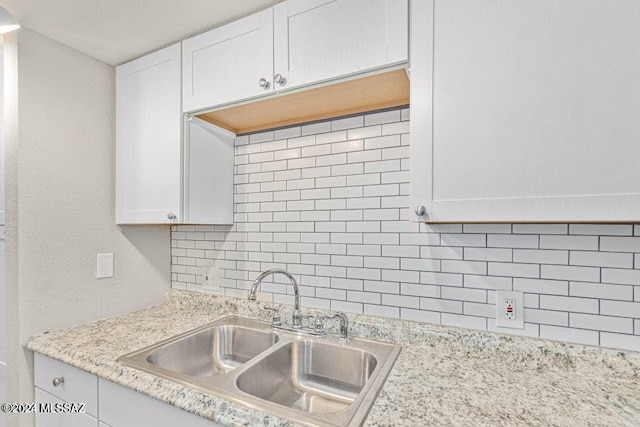 kitchen with light stone counters, decorative backsplash, sink, and white cabinets