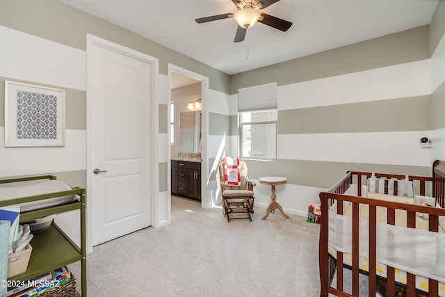 bedroom featuring ceiling fan, light carpet, ensuite bath, and a crib