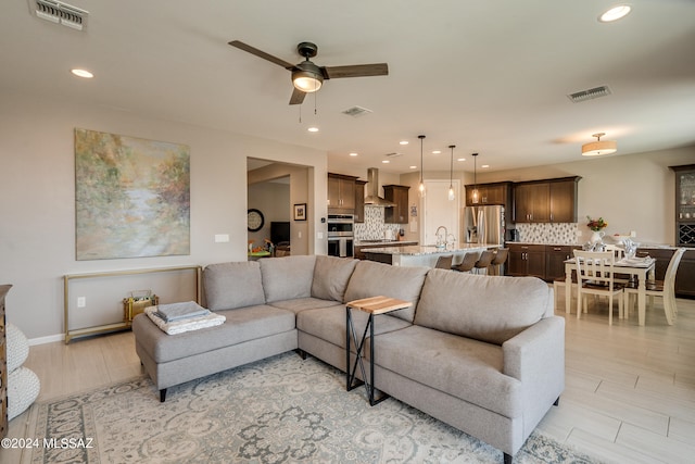 living room featuring light wood-type flooring, ceiling fan, and sink