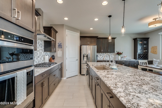 kitchen with sink, dark brown cabinets, decorative light fixtures, wall chimney exhaust hood, and appliances with stainless steel finishes