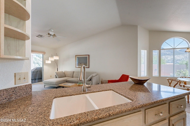 kitchen with lofted ceiling, light stone counters, ceiling fan, and sink