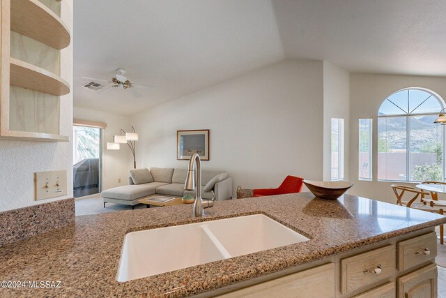 kitchen featuring lofted ceiling, a sink, light stone counters, and open floor plan