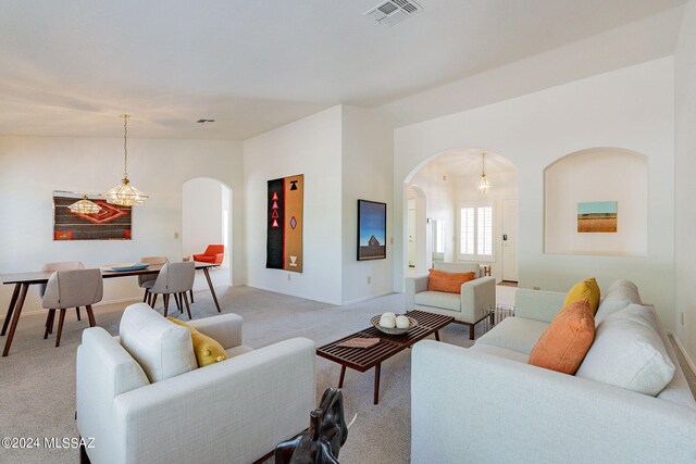 living area featuring visible vents, arched walkways, a notable chandelier, and light colored carpet