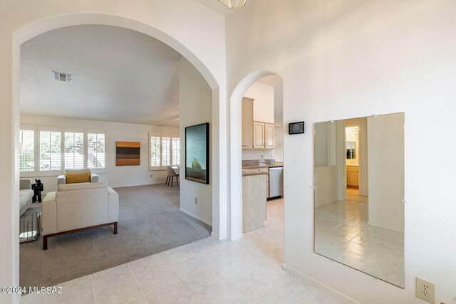 hall with visible vents, baseboards, light tile patterned flooring, light carpet, and a high ceiling