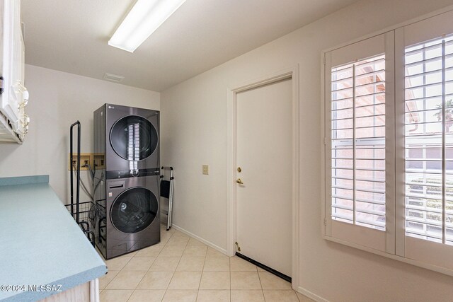 laundry area with light tile patterned flooring, stacked washer and clothes dryer, laundry area, and baseboards