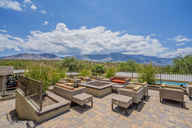 view of patio with fence, an outdoor living space with a fire pit, and a mountain view