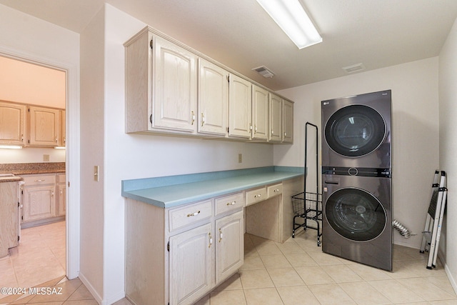 clothes washing area featuring stacked washer and clothes dryer, light tile patterned flooring, and cabinets