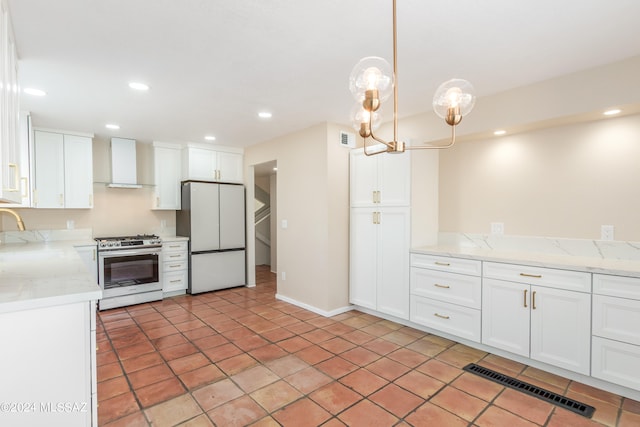 kitchen with white refrigerator, stainless steel range with gas stovetop, white cabinets, and wall chimney exhaust hood