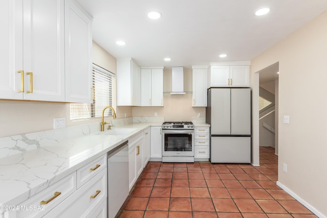 kitchen featuring wall chimney range hood, sink, light stone counters, appliances with stainless steel finishes, and white cabinetry