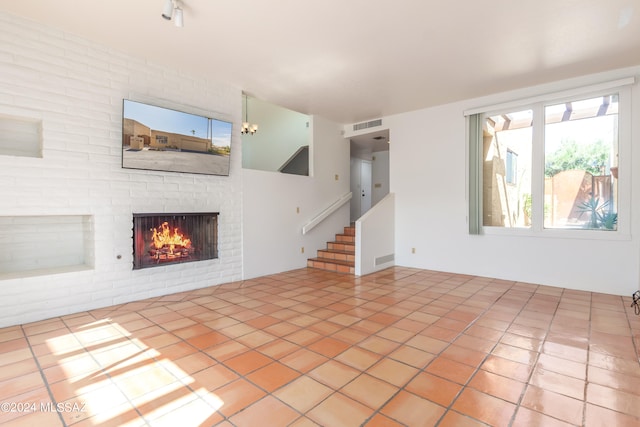 unfurnished living room with light tile patterned flooring, a brick fireplace, and an inviting chandelier