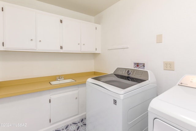 clothes washing area with washing machine and dryer, cabinets, and sink