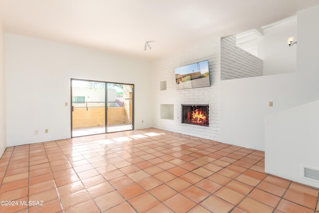 unfurnished living room featuring light tile patterned flooring, a brick fireplace, and a high ceiling