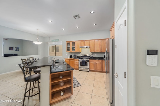kitchen with under cabinet range hood, light tile patterned flooring, appliances with stainless steel finishes, and a kitchen bar