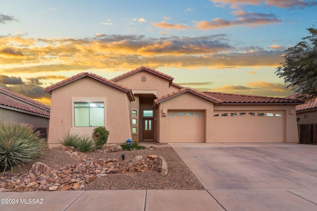 view of front of house featuring stucco siding, a tiled roof, driveway, and a garage
