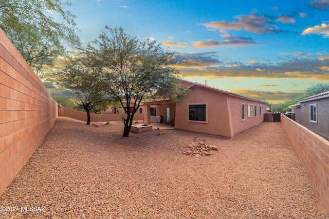 back of house at dusk with a tile roof, a fenced backyard, and stucco siding
