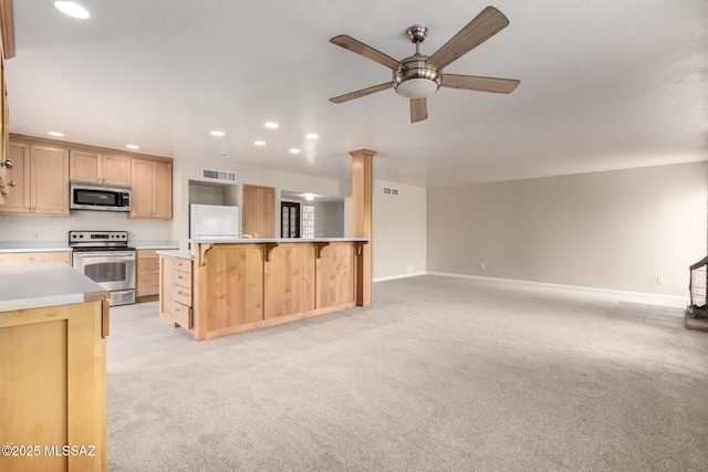 kitchen with appliances with stainless steel finishes, a breakfast bar, light colored carpet, and light brown cabinetry