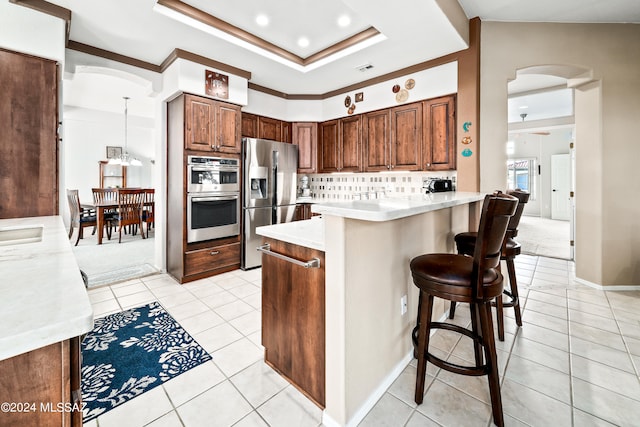 kitchen featuring stainless steel appliances, kitchen peninsula, backsplash, a breakfast bar, and decorative light fixtures