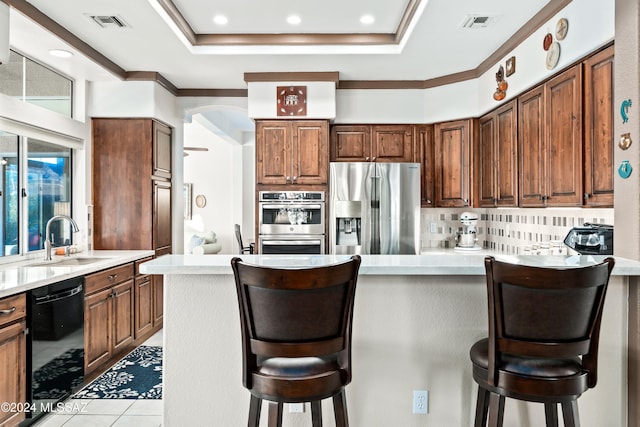 kitchen featuring a kitchen bar, sink, tasteful backsplash, a raised ceiling, and appliances with stainless steel finishes