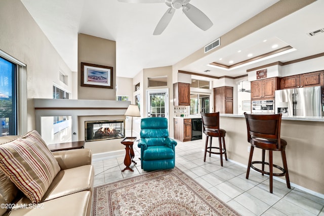 living room with light tile patterned floors, a multi sided fireplace, ceiling fan, crown molding, and a raised ceiling