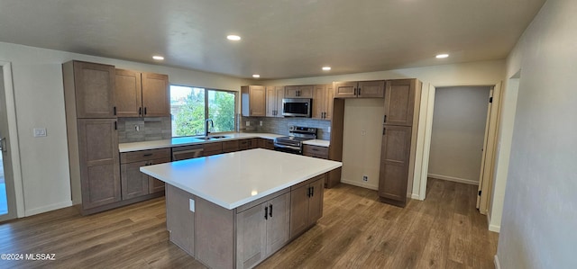 kitchen with appliances with stainless steel finishes, hardwood / wood-style floors, a center island, and backsplash