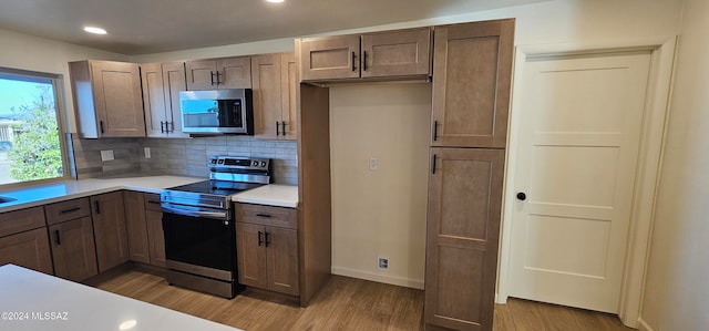 kitchen with decorative backsplash, appliances with stainless steel finishes, and light wood-type flooring