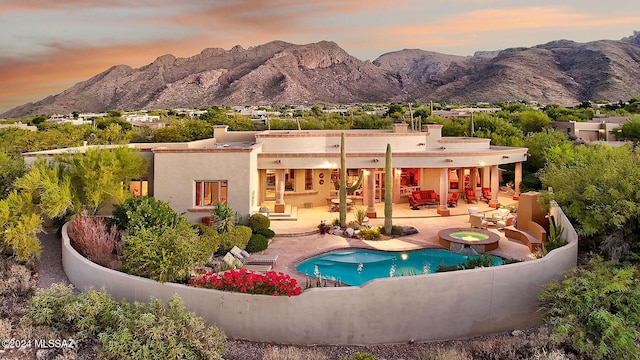 back house at dusk featuring a fenced in pool, a mountain view, a patio, and an outdoor living space