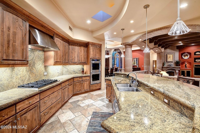 kitchen with ornate columns, sink, wall chimney exhaust hood, hanging light fixtures, and decorative backsplash