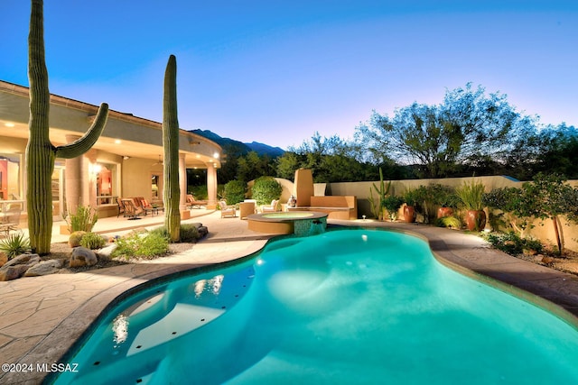 pool at dusk featuring a patio area and an in ground hot tub