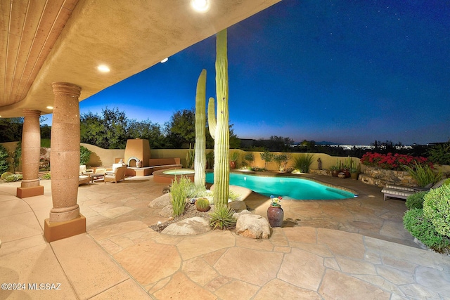 pool at dusk with exterior fireplace and a patio area