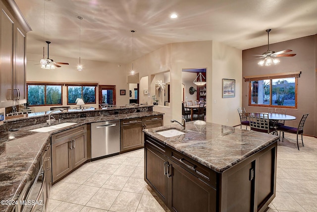 kitchen featuring stainless steel dishwasher, sink, a center island with sink, and dark stone counters