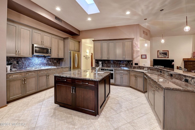 kitchen featuring sink, appliances with stainless steel finishes, a skylight, decorative light fixtures, and dark stone counters