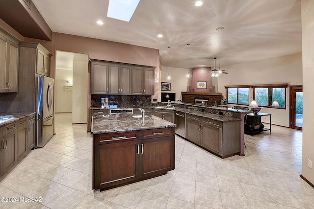 kitchen featuring a skylight, dark stone countertops, backsplash, kitchen peninsula, and stainless steel appliances