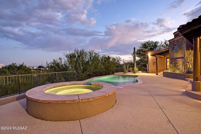 pool at dusk with a patio area and an in ground hot tub